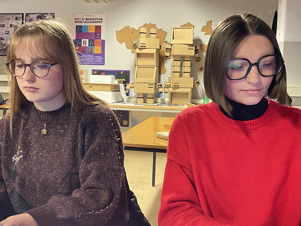 deux filles du groupe, l'une rousse avec de longs cheveux et l'autre avec un carré court et les cheveux bruns, travaillent et sont concentrées sur leur tâche